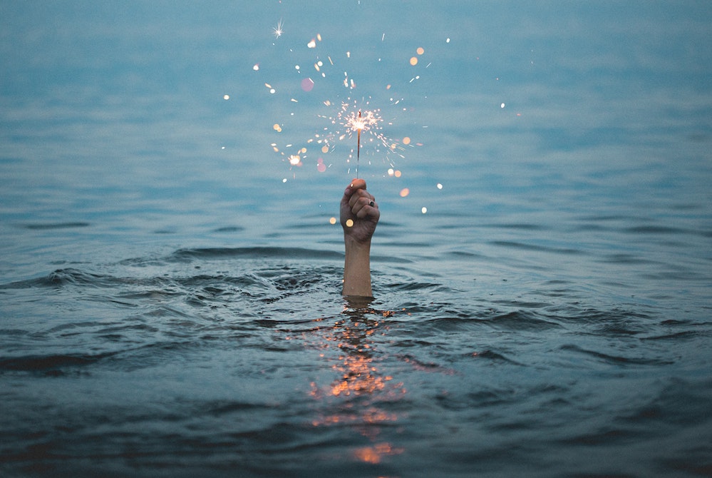 Image of a person holding a lit sparkler above the water (Unsplash/Kristopher Roller) Image of a person holding a lit sparkler above the water (Unsplash/Kristopher Roller)
