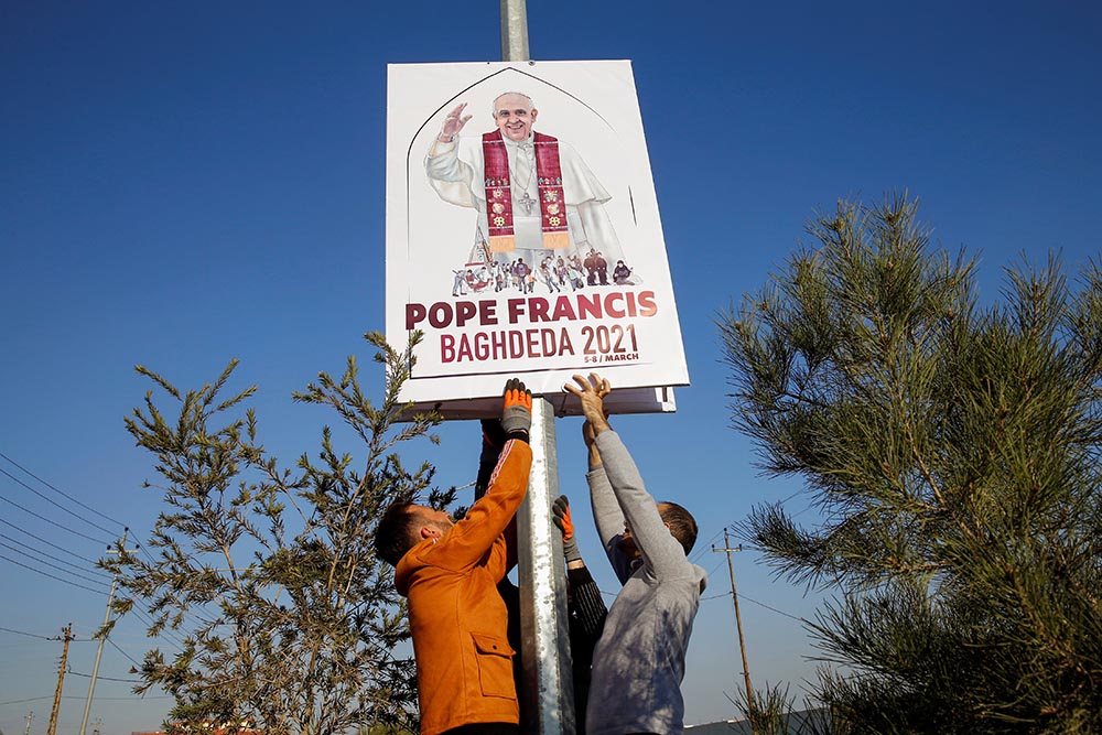 Volunteers secure a placard on a pole along a street in Qaraqosh, Iraq, Feb. 22. The placard shows the official logo, designed by Ragheed Nenwaya, for Pope Francis' planned March 7 visit to Qaraqosh, also known by its Aramaic name of Baghdeda. Volunteers secure a placard on a pole along a street in Qaraqosh, Iraq, Feb. 22. The placard shows the official logo, designed by Ragheed Nenwaya, for Pope Francis' planned March 7 visit to Qaraqosh, also known by its Aramaic name of Baghdeda.