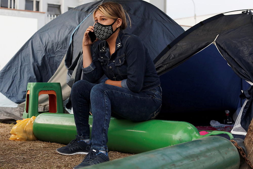 Yoselin Marticorena, 26, talks on her cellphone March 3 while sitting outside a tent on the grounds of Hospital Villa El Salvador in Lima, Peru. She was living in the tent while waiting for information regarding the health of her father, who was hospitali Yoselin Marticorena, 26, talks on her cellphone March 3 while sitting outside a tent on the grounds of Hospital Villa El Salvador in Lima, Peru. (CNS/Reuters/Angela Ponce)