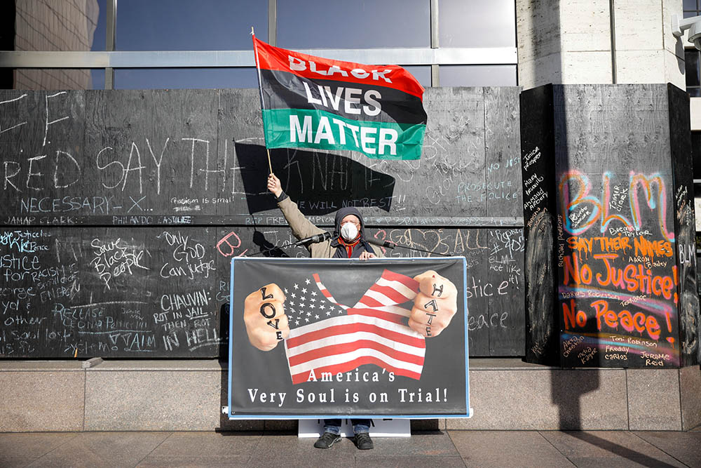 A demonstrator holds a Black Lives Matter flag and another sign April 6 outside the Hennepin County Government Center in Minneapolis on the seventh day of the trial of former police officer Derek Chauvin. (CNS/Reuters/Nicholas Pfosi) A demonstrator holds a Black Lives Matter flag and another sign April 6 outside the Hennepin County Government Center in Minneapolis on the seventh day of the trial of former police officer Derek Chauvin. (CNS/Reuters/Nicholas Pfosi)