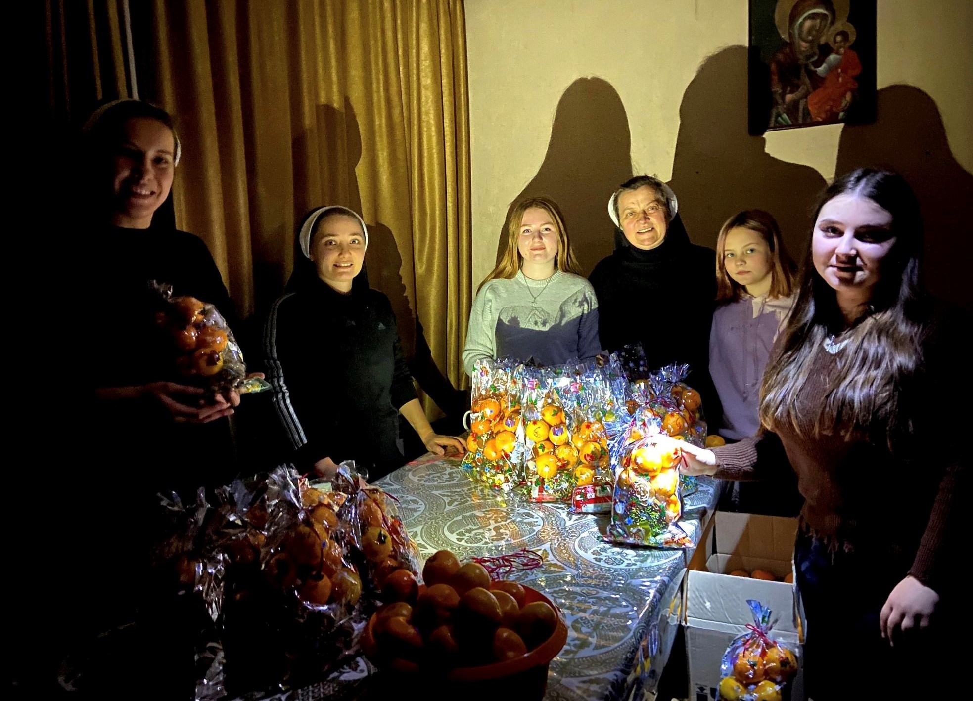 Basilian Sisters and young people prepare for St. Nicholas Day during a blackout in eastern Ukraine on Dec. 19, 2022, the feast of St. Nicholas. They are around a table with holiday food and they cast shadows on the walls. calendar, which Ukraine follows. (