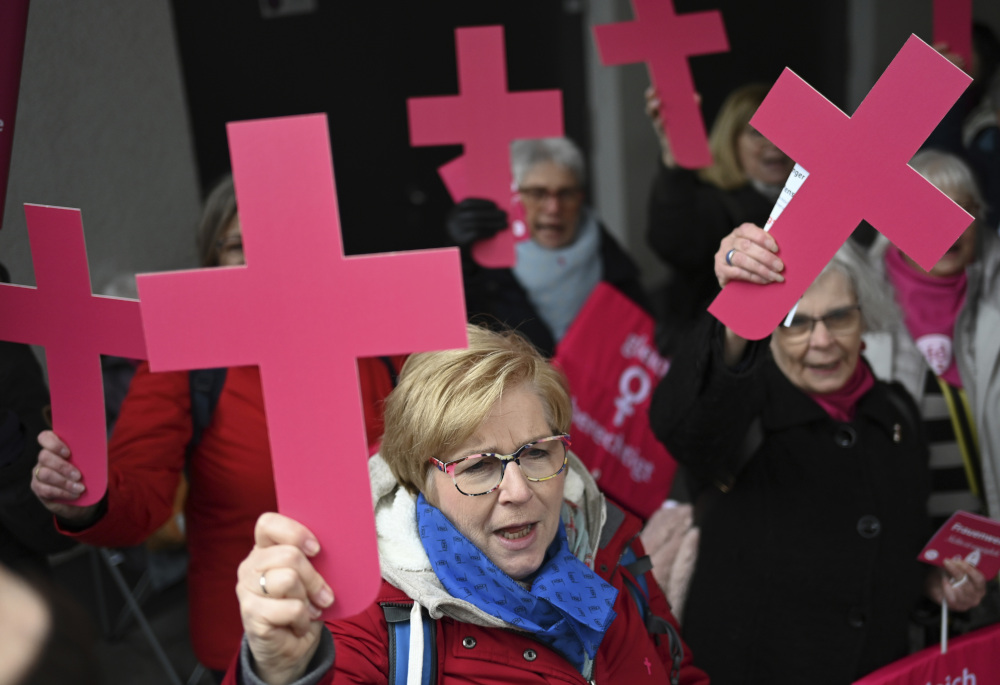 Women, wearing winter coats, energetically hold pink crosses above their heads