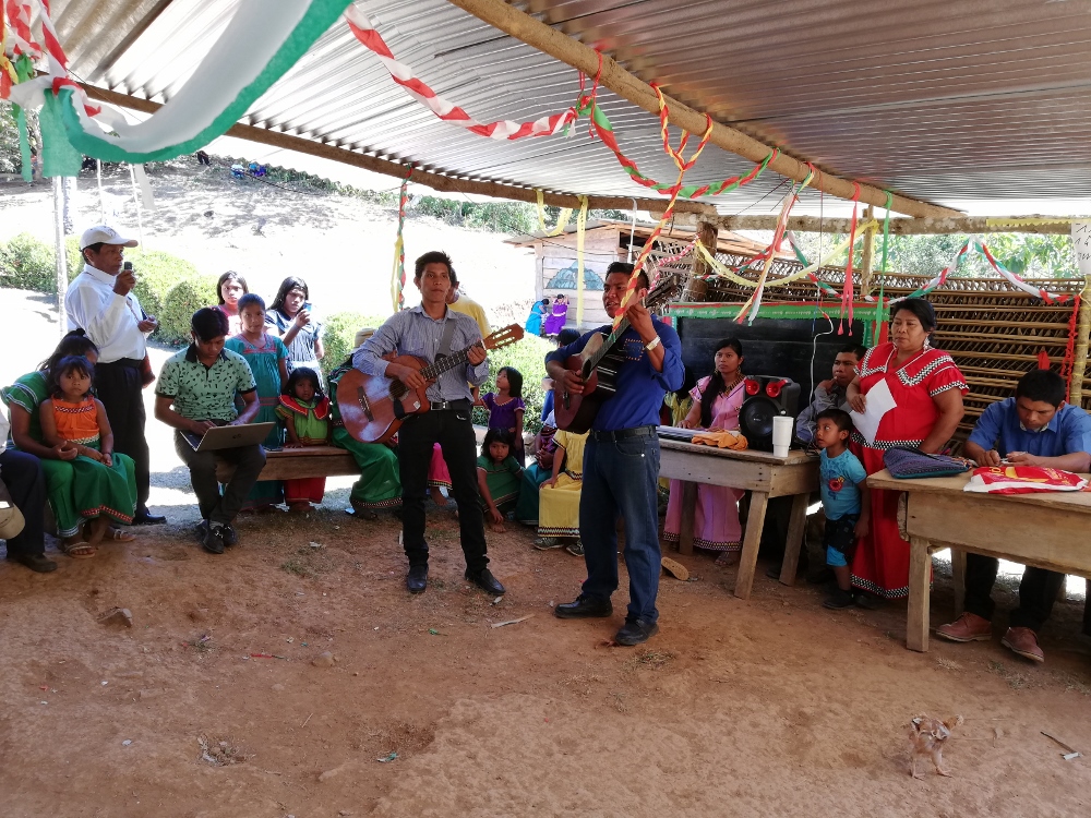 Under a bohío, a young man with a guitar sings to an indigenous assembly."