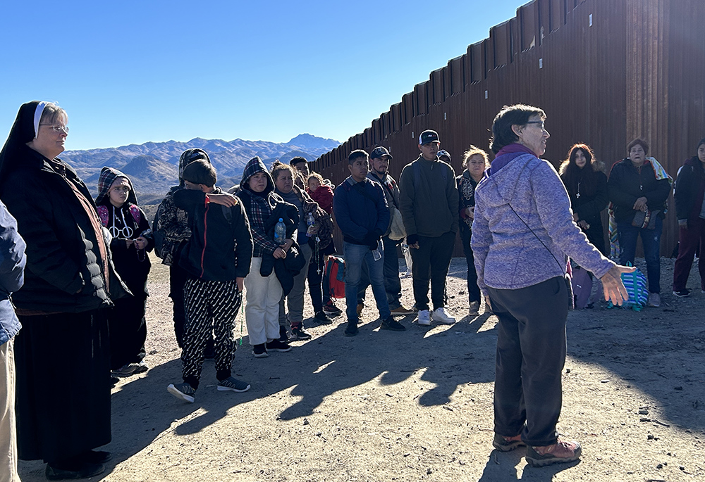 Sr. Judy Bourg (purple jacket) stands with asylum-seekers who entered the United States through an opening in the U.S.-Mexico border wall. Bourg welcomed each of them, then gathered them in a circle, and said, "We are happy that you are here." To Bourg's left is Sr. Maria Louis Edwards. (Peter Tran)