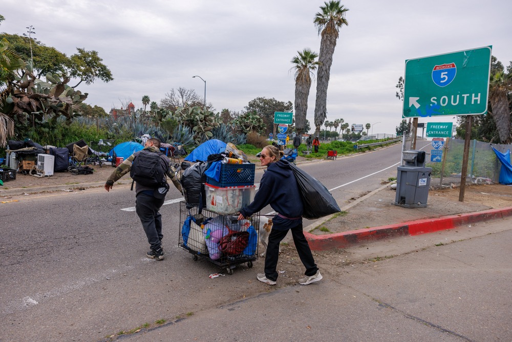 Supreme Court, homeless sleeping case Two people push a cart filled with items across freeway toward encampment