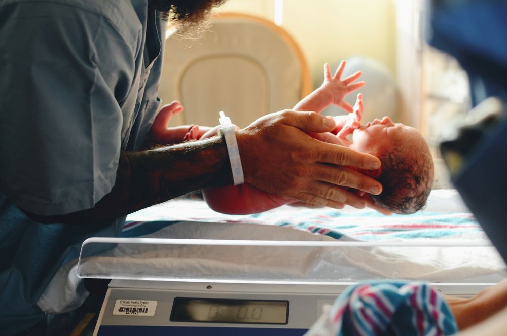 Person holds baby in hospital ward.