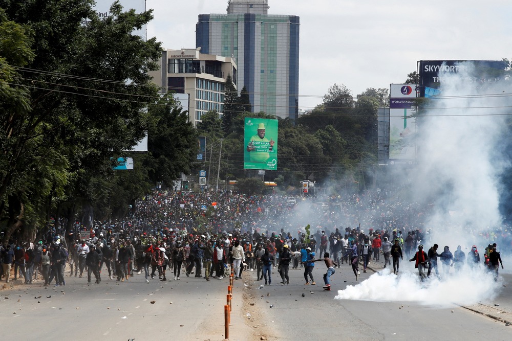 Kenyan finance bill protests 2024 Enormous assembly marches through wide boulevard as smoke rises from street.