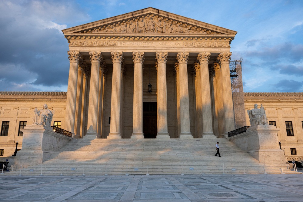 U.S Supreme Court building. Courthouse looms in the evening light; security guard, dwarfed by building, walks down the stairs.