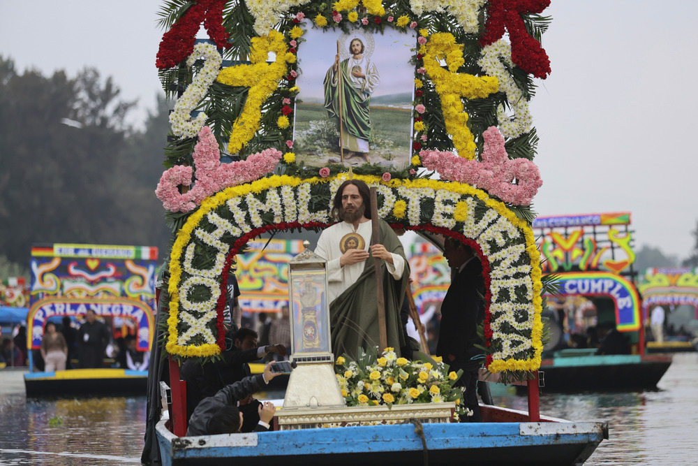 Floating procession with relic of St. Jude, Xochimilco canals, Mexico City, Sunday, Aug. 11, 2024. Man dressed as St. Jude Thaddeus, stands on front of decorated barge, floating down river and carrying a relic of St. Jude.