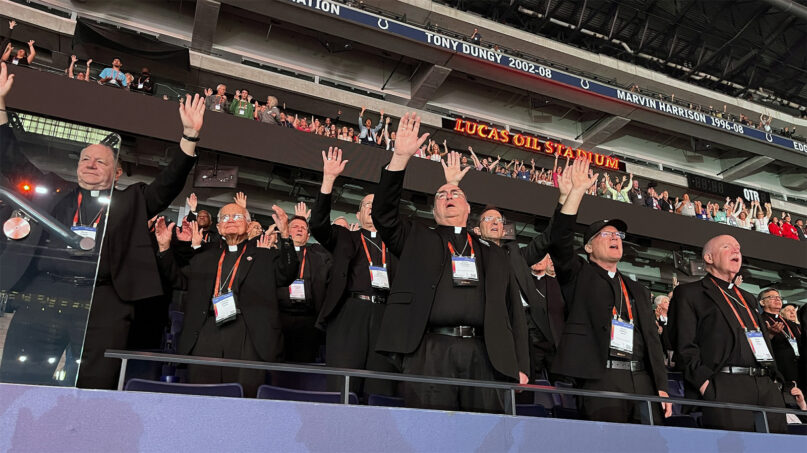 National Eucharistic Congress, July 20, 2024. Bishops wearing plain black clerics stand with hands raised.