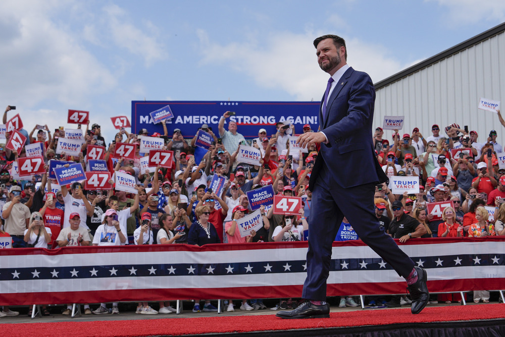JD Vance, Asheboro, North Carolina, Aug. 21, 2024. Vance walks across red-carpeted platform; in background, supporters in stands hold signs.