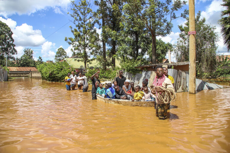 Floodwaters, Nairobi, Kenya, April 24, 2024. People on boat, and others wading through flooded street.
