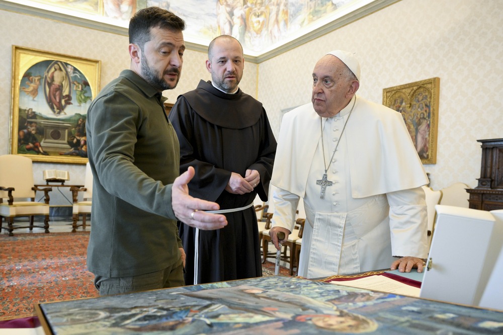 Francis and Zelenskyy third post-invasion meeting, Vatican, Oct. 11, 2024. Francis, Zelenskyy, and a monk bend over a desk in the apostolic library to regard Zelenskyy's gift of an oil painting.