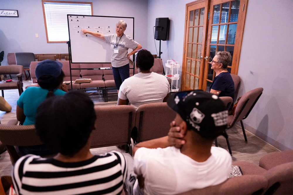 English class for Haitian immigrants, Springfield, Ohio, Sept. 13, 2024. Kaufman stands in front of whiteboard, people sit in chairs listening.