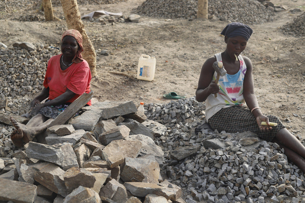 South Sudanese refugees, Palabek Refugee Settlement, northern Uganda. Two women sit on a pile of rocks holding mallets.