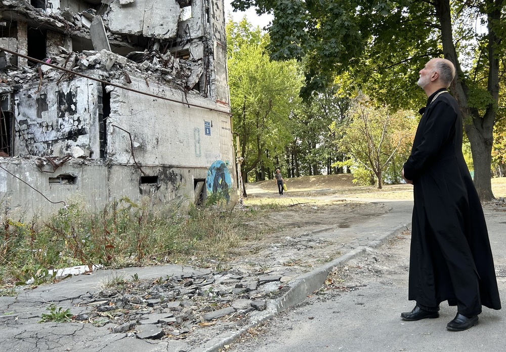 Archbishop A. Gudziak of the Ukrainian Greek Catholic Archeparchy of Philadelphia, Kharkiv, Ukraine, Sept. 8, 2024. The archbishop wears plain black cassock, and stands back regarding ruins of building.