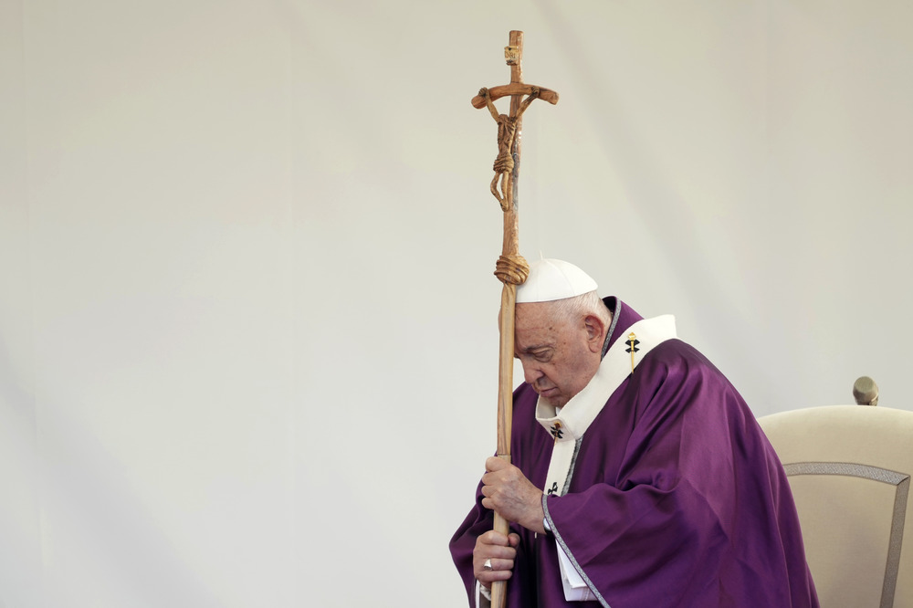 Pope Francis, All Souls Mass, Laurentino cemetery, Nov. 2, 2024. Pope, vested in penitential purple, stands, and leans head on processional cruxifix.