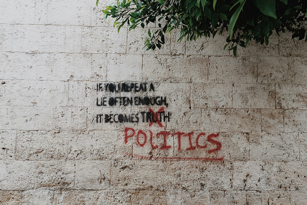 Grafitti on a white brick wall that says "If you repeat a lie often enough, it becomes politics" (Unsplash/Brian Wertheim)