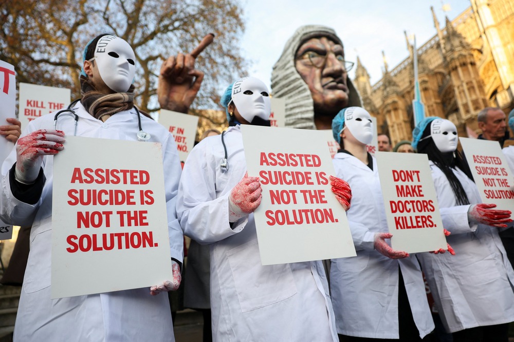 Anti-euthanasia protesters, Nov. 29, 2024, London. Masked protesters wear white medical coats and hold signs reading "Assisted suicide is not the solution."