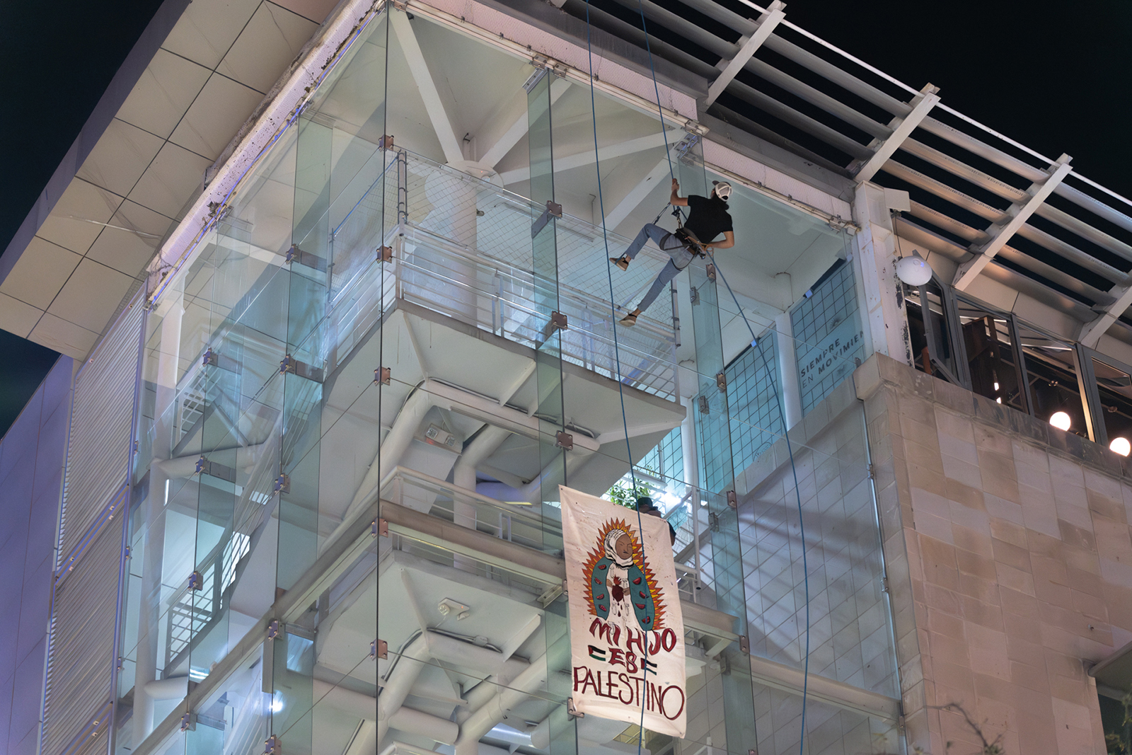 Guadalupe Palestinian solidarity display, Chihuahua, Mexico. Person on rope against tall building, banner hangs.