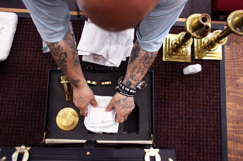 Inmate helping at Mass, Ellsworth Correctional Facility, Kansas. Only the inmate's arms and hands are visible, from above, folding a small altar cloth.