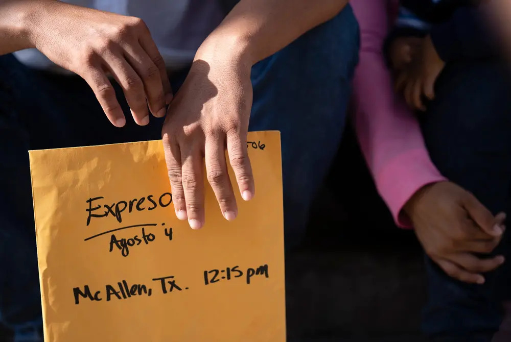 Migrants, Catholic Charities Humanitarian Respite Center, McAllen, Texas, Aug. 2, 2021. Only Ledezma's hands are shown, holding folder.