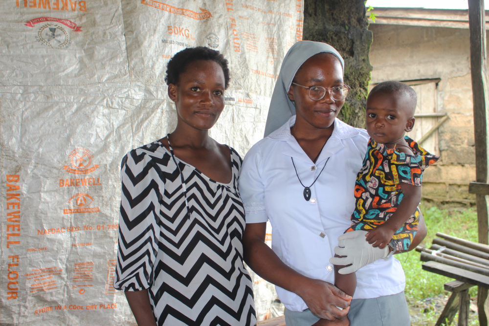 Sr. Janefrances Ihekuna holding a baby Sr. Janefrances Ihekuna (right) poses for a photo with a nursing mother and her baby after testing them for malaria and HIV during free medical outreach in the community.