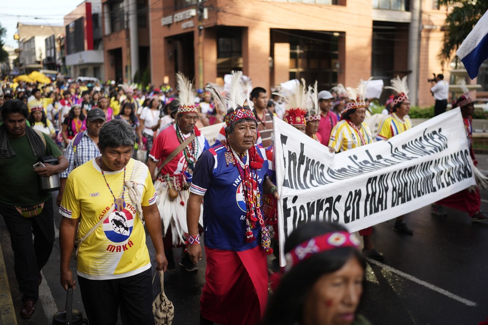 Maka indigenous marching for land rights, Asuncion, Paraguay, Feb. 28, 2024. People in traditional garments march through streets behind banner.