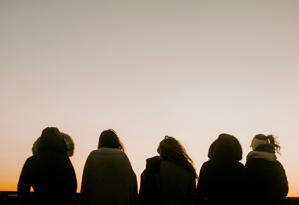 A group of people, backs turned, face toward a foggy horizon in an outdoor setting. (Unsplash/Annie Williams)