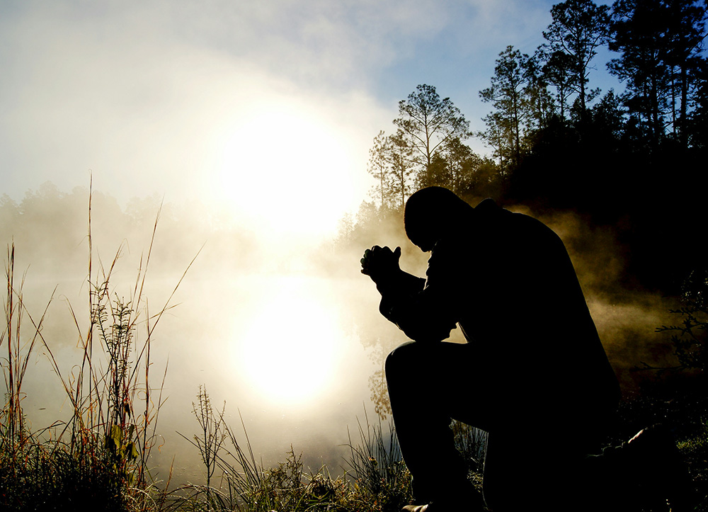 A man praying beside a lake (Unsplash/Aaron Burden)