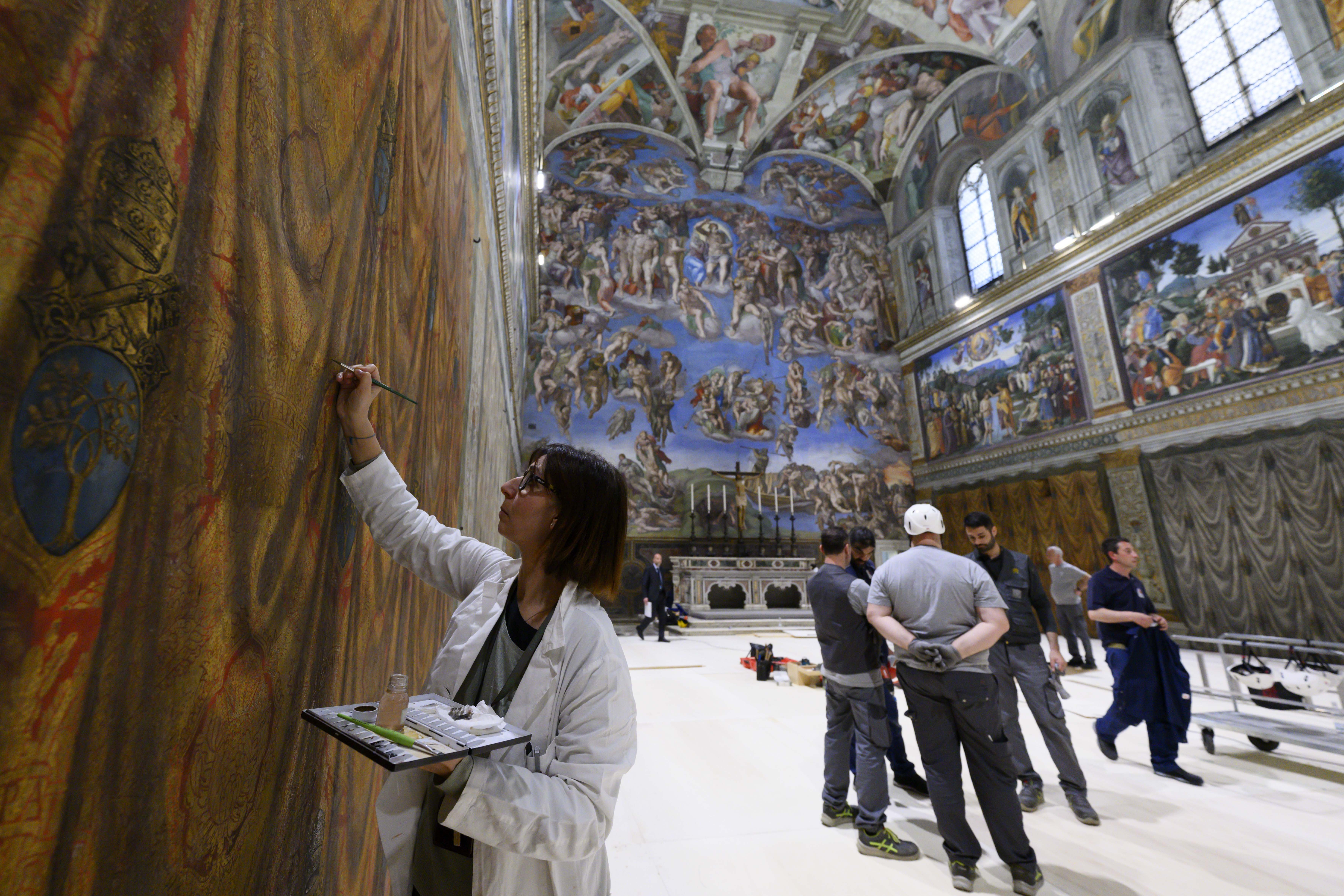 As a restorer with the Vatican Museums touches up a wall fresco in the Sistine Chapel at the Vatican May 2, 2025, workers prepare to build platforms over a protective covering on the marble floor May 2, 2025. The cardinals who enter the conclave to elect a new pope May 7 will sit at tables facing the center of the chapel with the tables in the back row raised slightly. (CNS photo/Vatican Media)