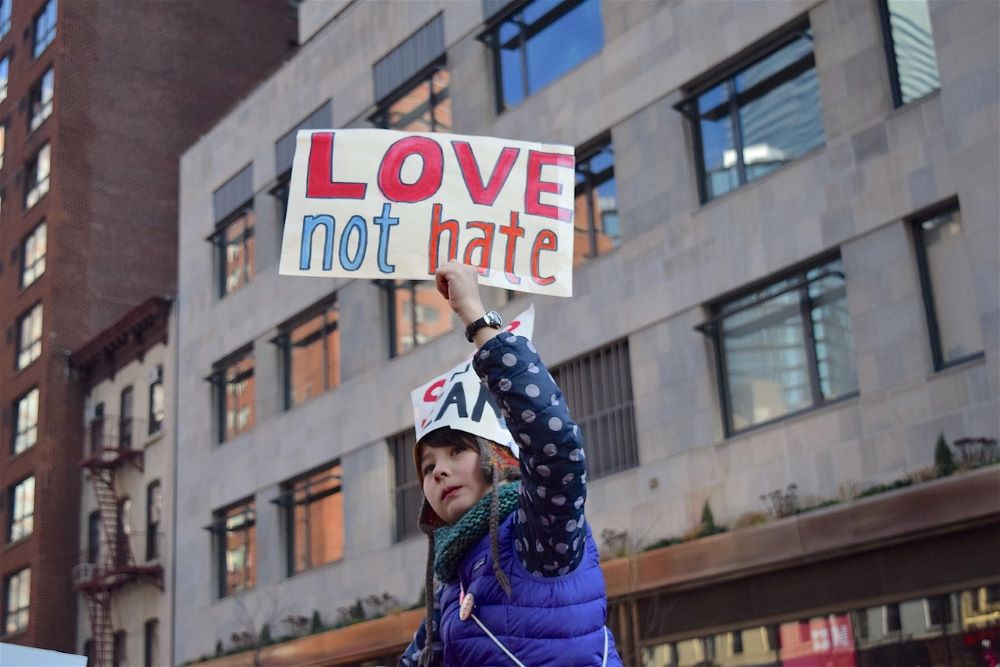 Woman holds sign: Love not hate.