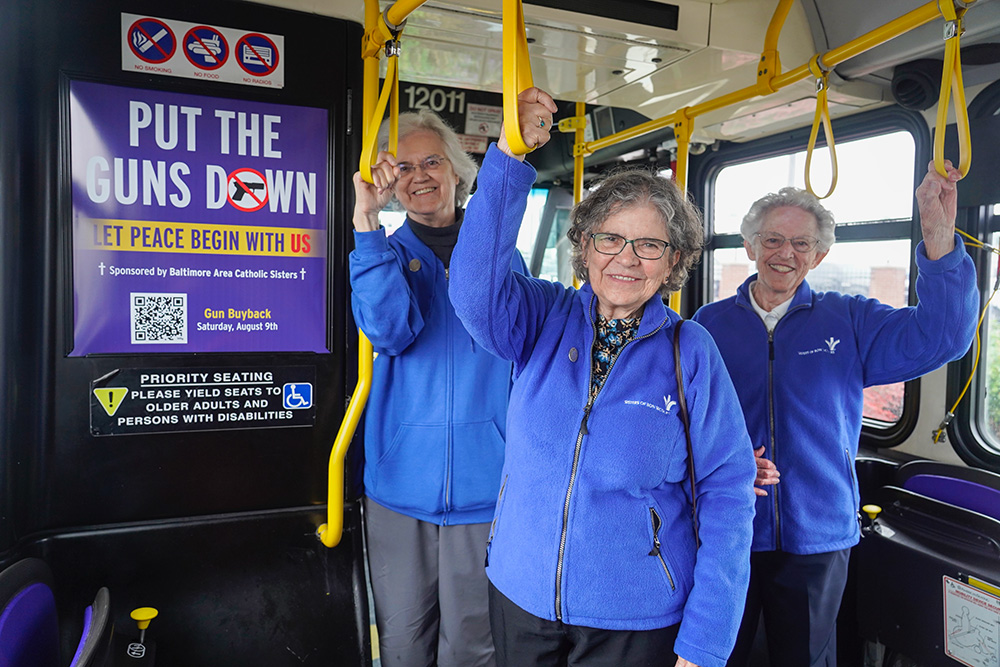 From left: Bon Secours Srs. Pat Dowling, Elaine Davia and Nancy Glynn stand beside an ad reading, "Put the Guns Down. Let Peace Begin with Us," inside a Baltimore city bus. The ad campaign runs through June on the outside and inside of city buses, and on Baltimore's subway. (Courtesy of Sisters of Bon Secours)