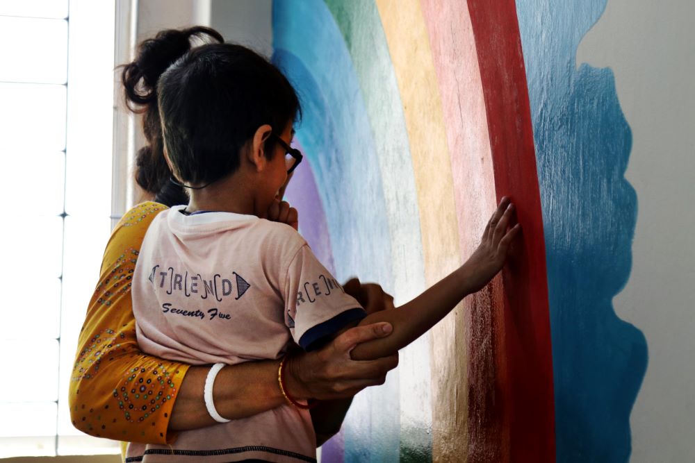 Volunteer with child and rainbow painted on wall. Volunteer with child and rainbow painted on wall.