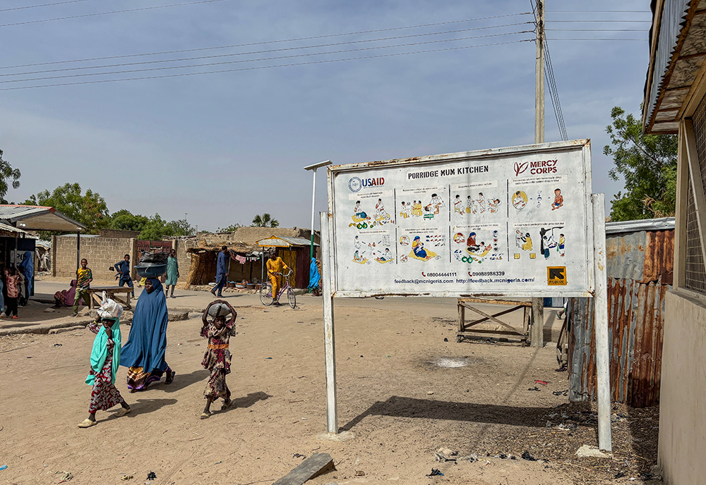 A woman and her children walk past a sign for a U.S. Agency for International Development program in Dikwa, Nigeria, April 29, 2025. (AP/Sunday Alamba)