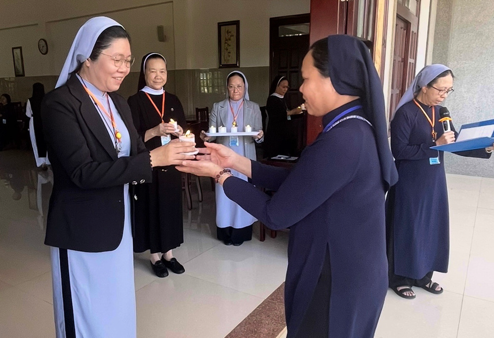 Sr. Maria Ly Thi Bich Quyen, left, offers a candle to a sister during the opening ceremony of the sabbatical on March 18 at the Rosary Retreat House in Lam Dong province. (Courtesy photo)