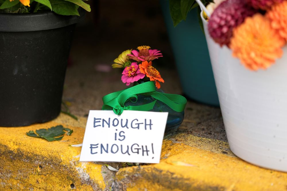 A sign reading "Enough is enough" stands amid flowers at a memorial at Annunciation Catholic Church. A sign reading "Enough is enough" stands amid flowers at a memorial at Annunciation Catholic Church.