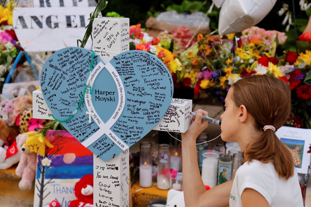 A child writes a message as people at a makeshift memorial. A child writes a message as people at a makeshift memorial.