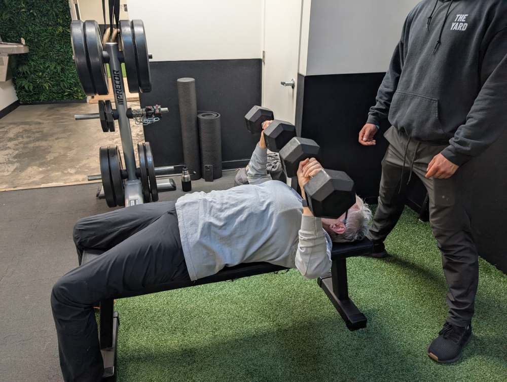 Sr. Pat Farrell lifts two 30-pound dumbbells Sr. Pat Farrell lifts two 30-pound dumbbells while Jake Levine, a trainer at The Yard gym, spots her.