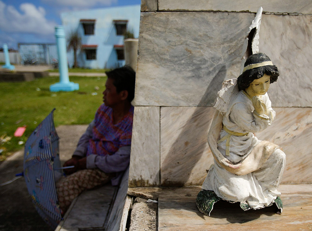 A woman sits in the shade alongside a broken angel statue near the destroyed cathedral in the typhoon-devastated waterfront town of Guiuan, Philippines, Nov. 19, 2013. (CNS/Reuters/Wolfgang Rattay)