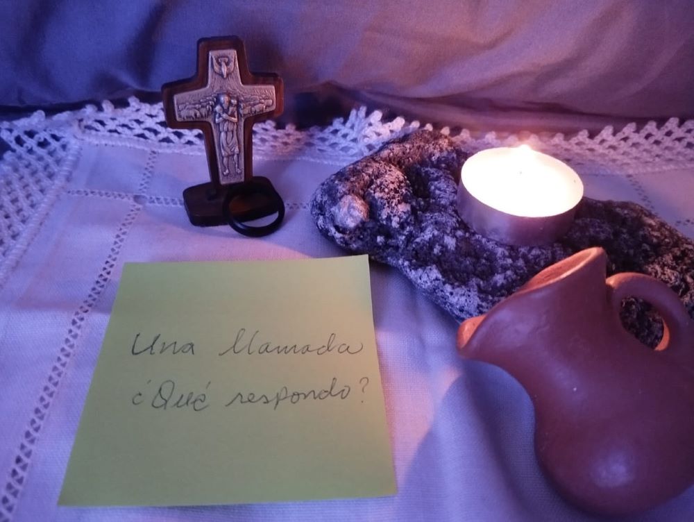 A cross, a clay jug and a candle sit beside a note in Spanish reading, "A call…how shall I respond?" (Flight in V)