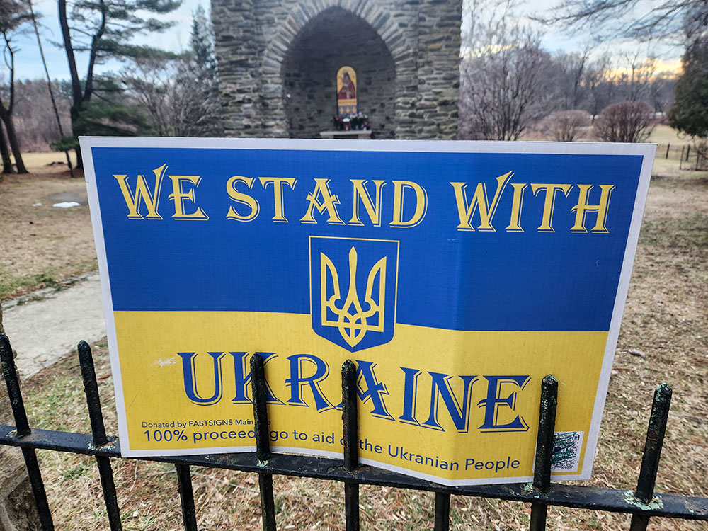 In Jenkintown, Pa., placards emblazoned with the national colors of yellow and blue declare support for Ukraine on a fence surrounding a grotto on the Basilian motherhouse grounds — the centerpiece being a shrine bearing the image of the Lady of Pochayiv, a revered sacred icon in Ukraine. (GSR photo/Chris Herlinger)