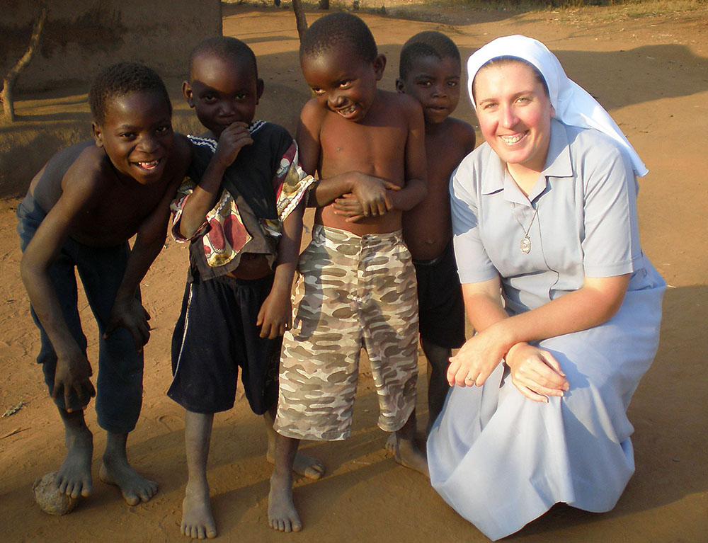 La hermana Dwyer en cuclillas junto a cuatro niños pequeños. Todos sonríen.