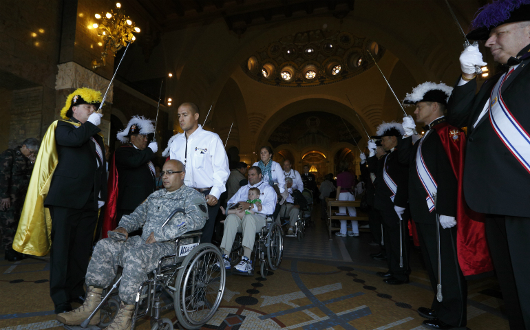 Members of the Knights of Columbus hold swords as U.S. military personnel leave in wheelchairs after a Mass at the Shrine of Our Lady of Lourdes in southwestern France May 16, 2014. About 60 wounded U.S. military personnel, together with family members and caregivers, were a part of the annual International Military Pilgrimage to Lourdes. (CNS photo/Paul Haring)