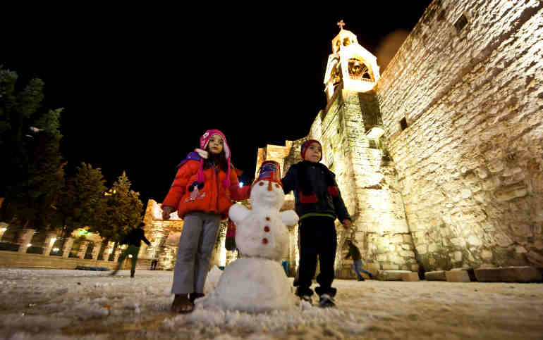 Children pose with a snowman outside the Church of the Nativity in the West Bank town of Bethlehem Jan. 9 during a rare cold spell. (CNS photo/Marcin Mazur, Bishops' Conference of England and Wales)