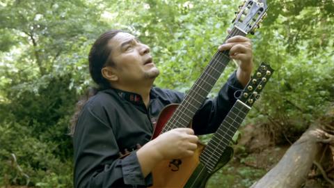 Sound of Silence, Our Father Man with long hair plays stringed instrument amidst greenery