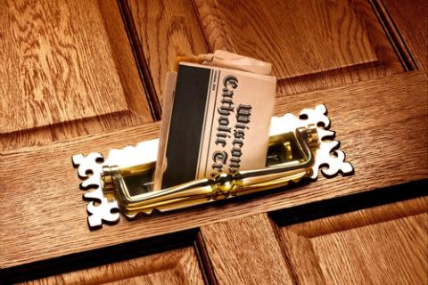 Newspaper peeks through front door mail slot.