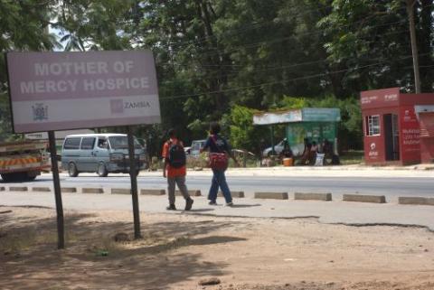 People walk on road near a sign for hospice.  People walk on road near a sign for hospice.