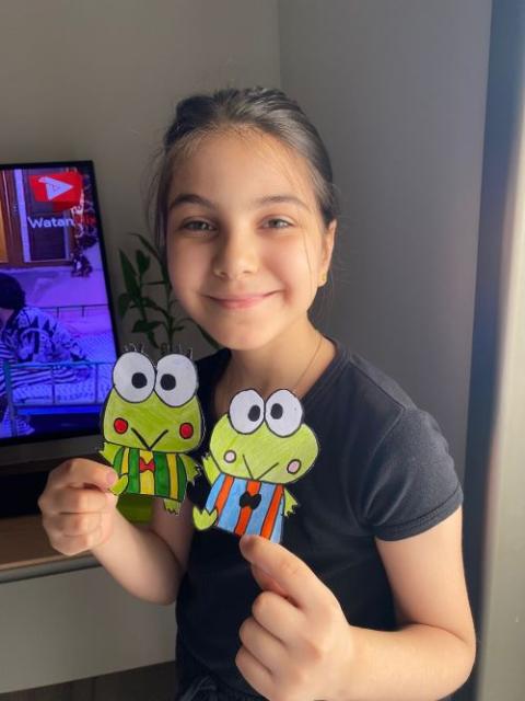 Girl holds drawings of frogs.