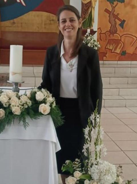 La hermana scalabriniana Nyzelle Dondé, de pie junto al altar, en donde reposan flores blancas y un cirio blanco.
